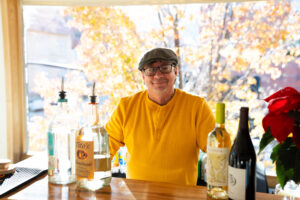 Bartender in bright yellow shirt at a sunny Boulder bar with autumn leaves outside — representing Boulder event venues and hospitality.