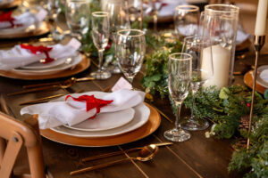 Holiday place setting at Wildflower Denver by KRUSH Photography with red ribbon on wine glass, napkin, holiday garland, wood table, and art gallery backdrop.